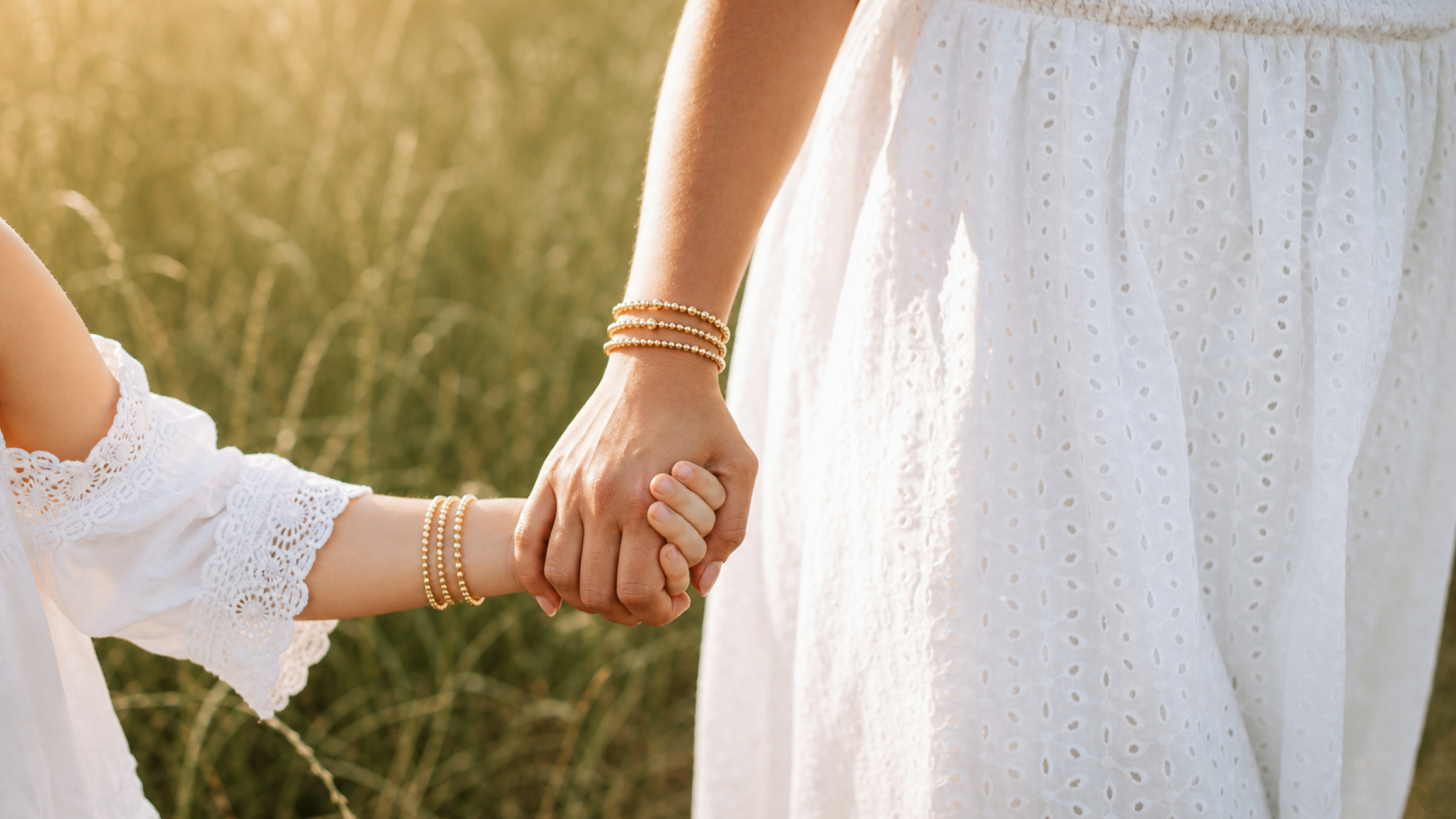 Mother and daughter holding hands, each wearing three matching Koen gold bracelets